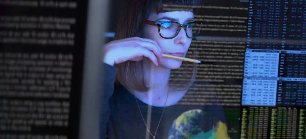 A person holding a pencil, reading a computer screen